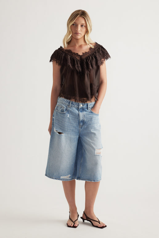 Woman wearing a dark brown lace ruffle top with flutter sleeves and light blue denim knee length shorts