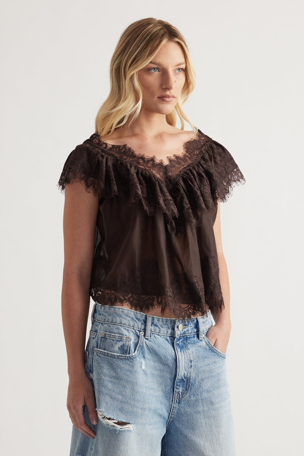 Woman wearing a black lace ruffle top with flutter sleeves and distressed blue jeans