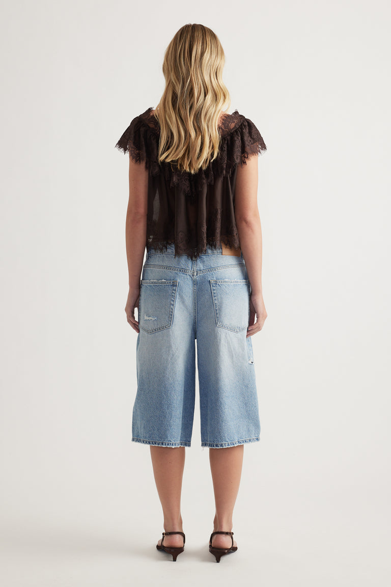 Girl viewed from behind wearing a dark lace ruffle top with flutter sleeves and light blue wide leg denim culottes