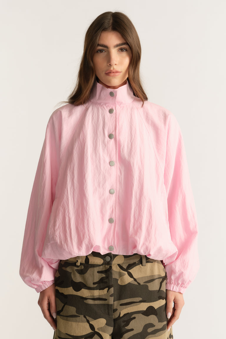 Woman wearing a lightweight pink funnel neck jacket with elastic cuffs and camouflage pants