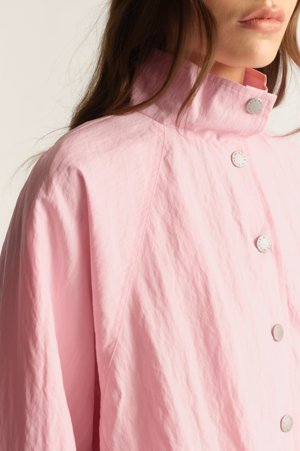 Woman wearing a pink lightweight funnel neck jacket with snap buttons