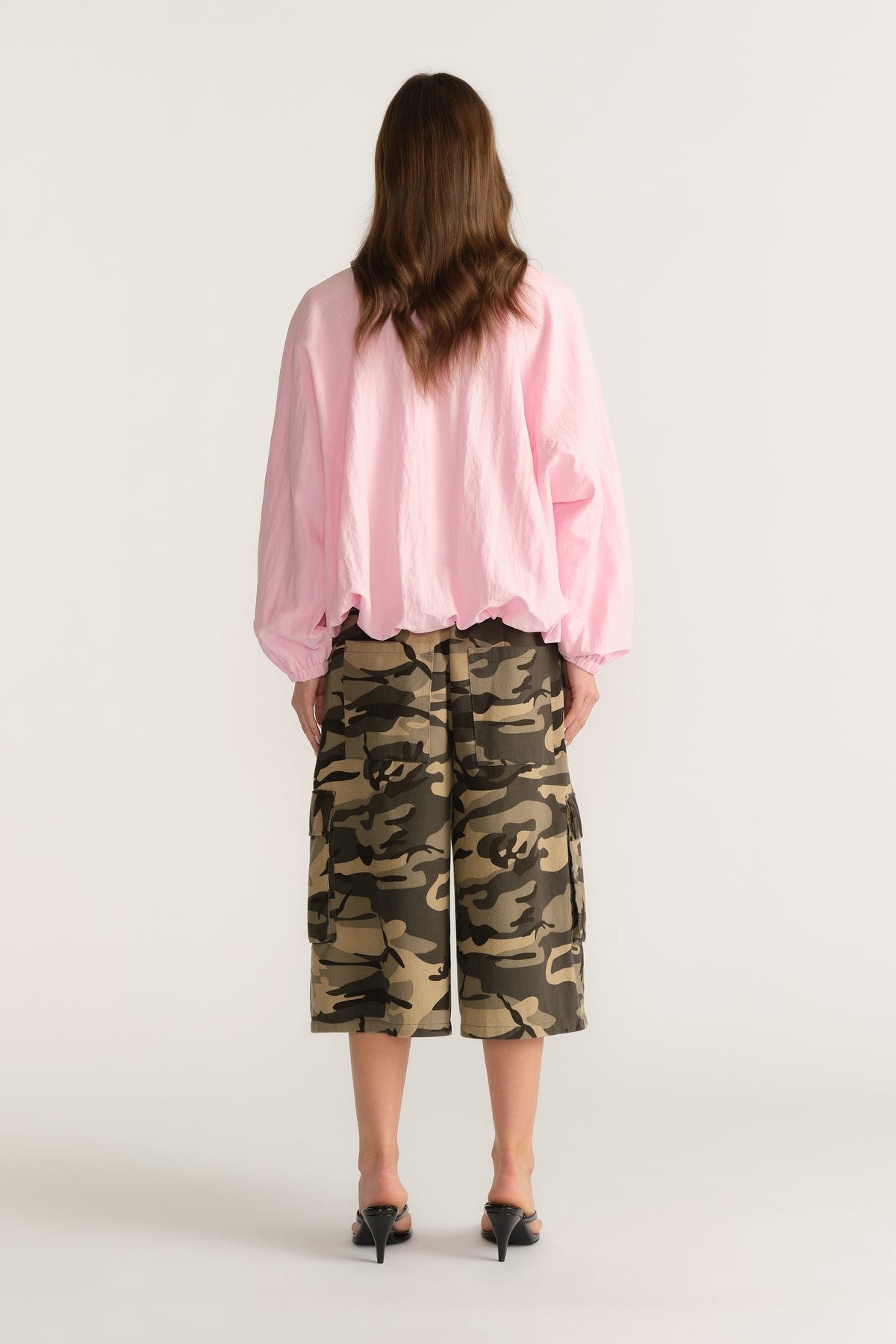 Woman wearing a lightweight pink jacket with camouflage knee length shorts, viewed from behind