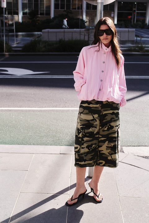 Woman wearing a pink lightweight jacket with camouflage shorts, sunglasses and black sandals