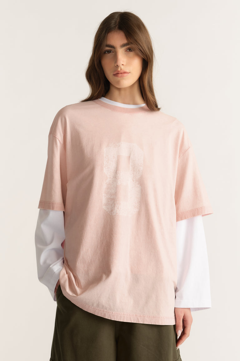 Model wearing an oversized washed pink tee over a white long sleeve top