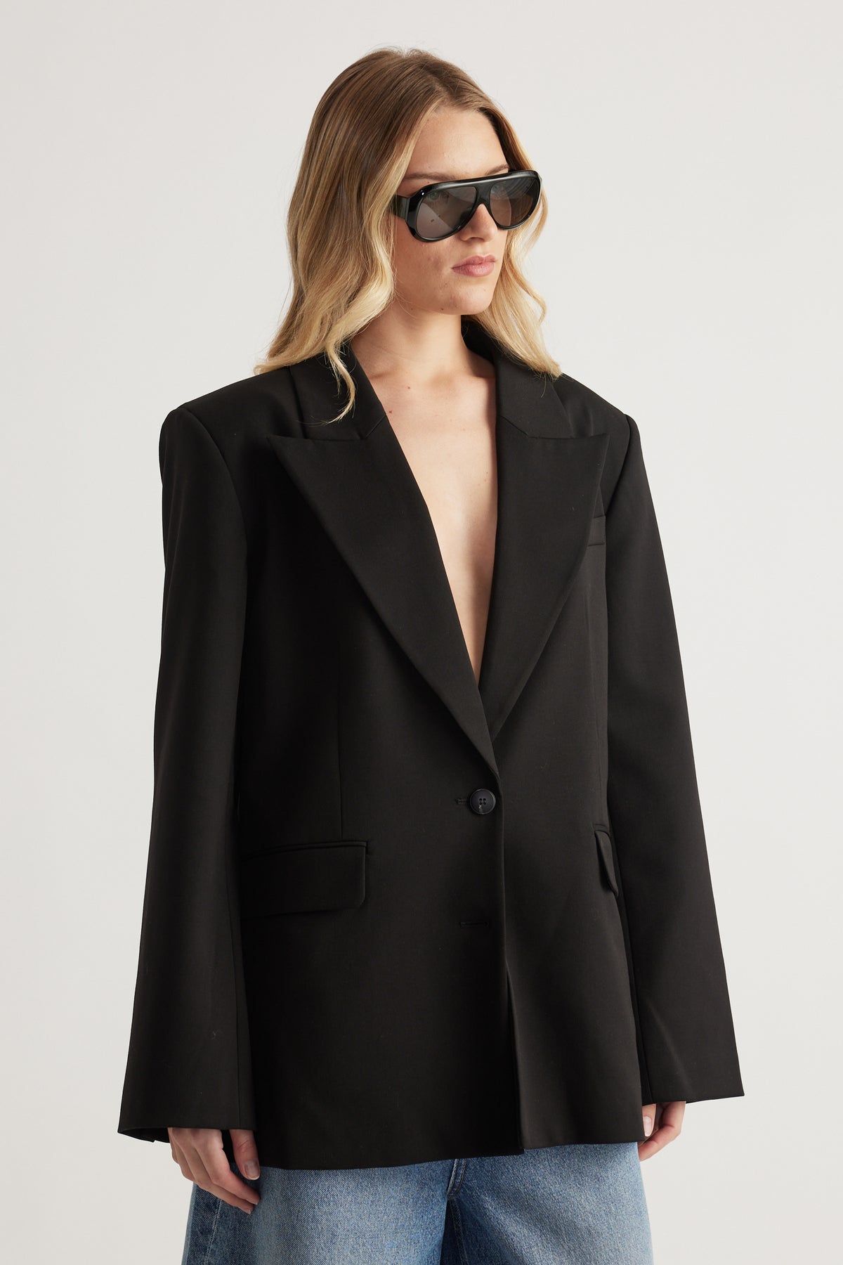 Woman wearing an oversized black blazer with front pockets, sunglasses and blue jeans
