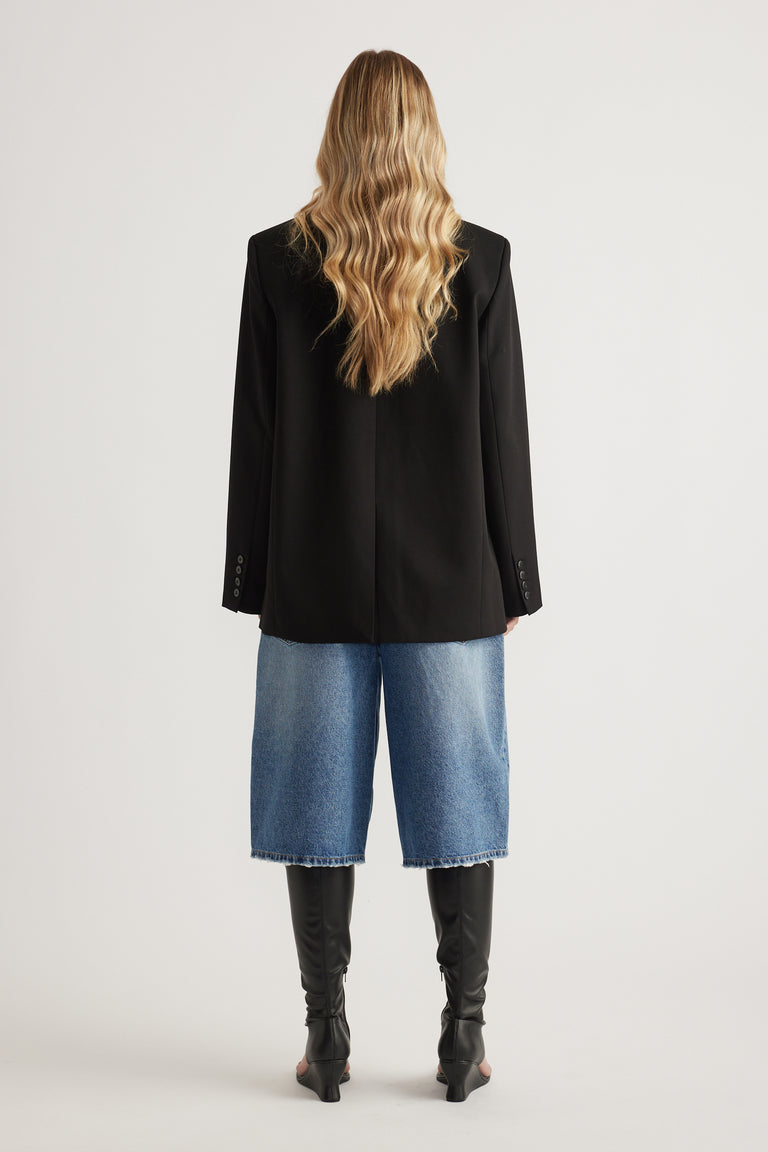 Back view of woman wearing an oversized black blazer with blue wide leg jeans and knee high boots