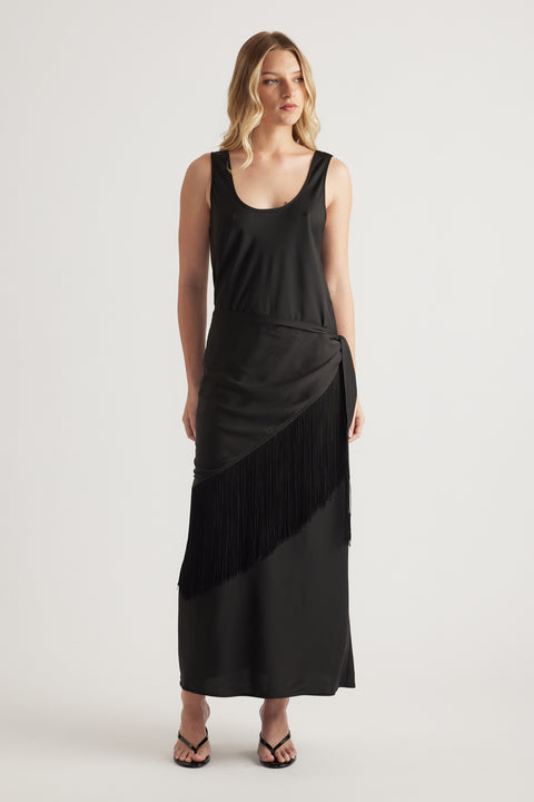 Woman wearing a black sleeveless maxi dress with a fringe waist and strappy sandals