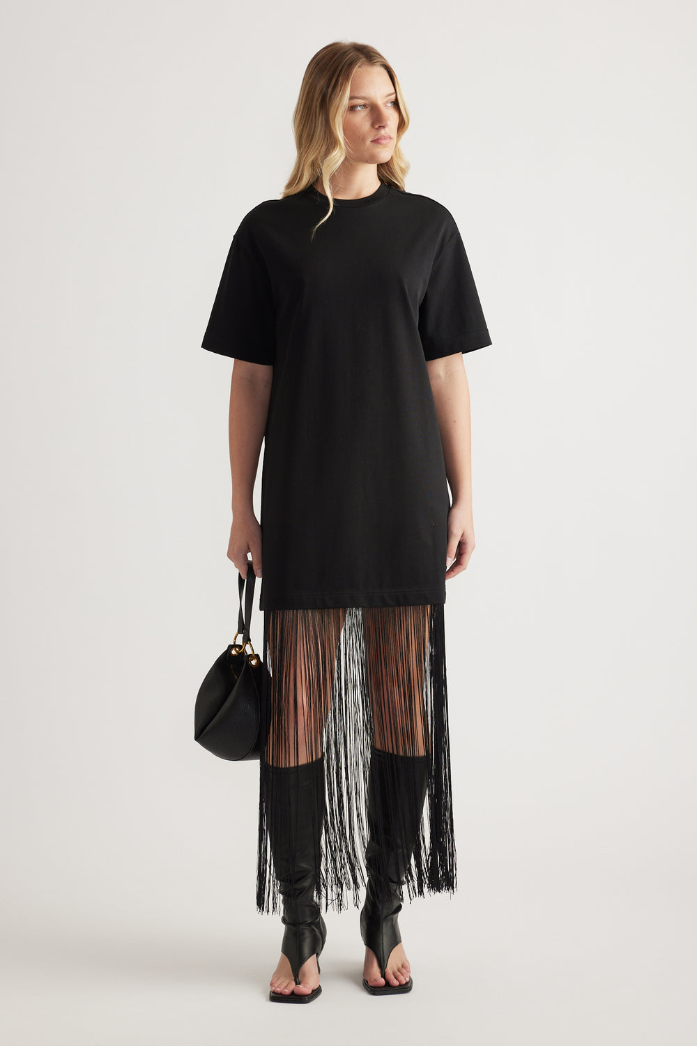 Woman wearing a black short sleeve maxi dress with a fringe hem and carrying a handbag