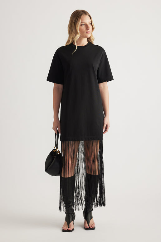 Woman wearing a black short sleeve maxi dress with a fringe hem and carrying a handbag