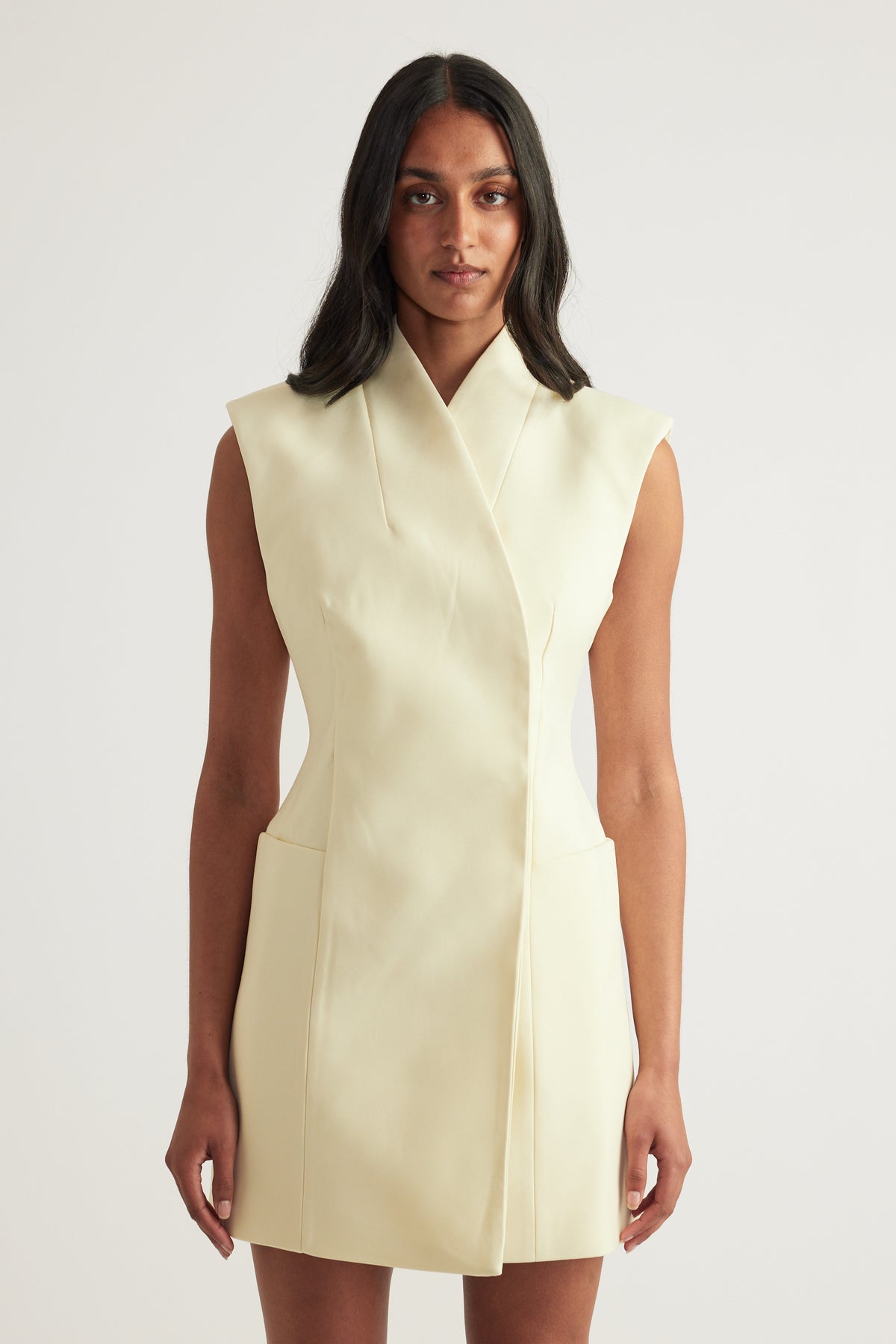 Woman wearing a cream sleeveless high neck structured mini dress with front pockets
