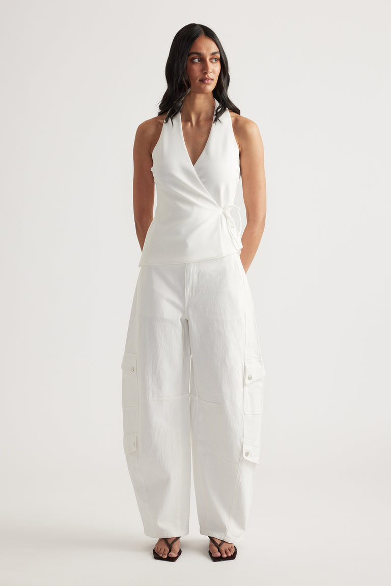 Woman wearing a white sleeveless wrap top with white cargo barrel leg jeans and black sandals
