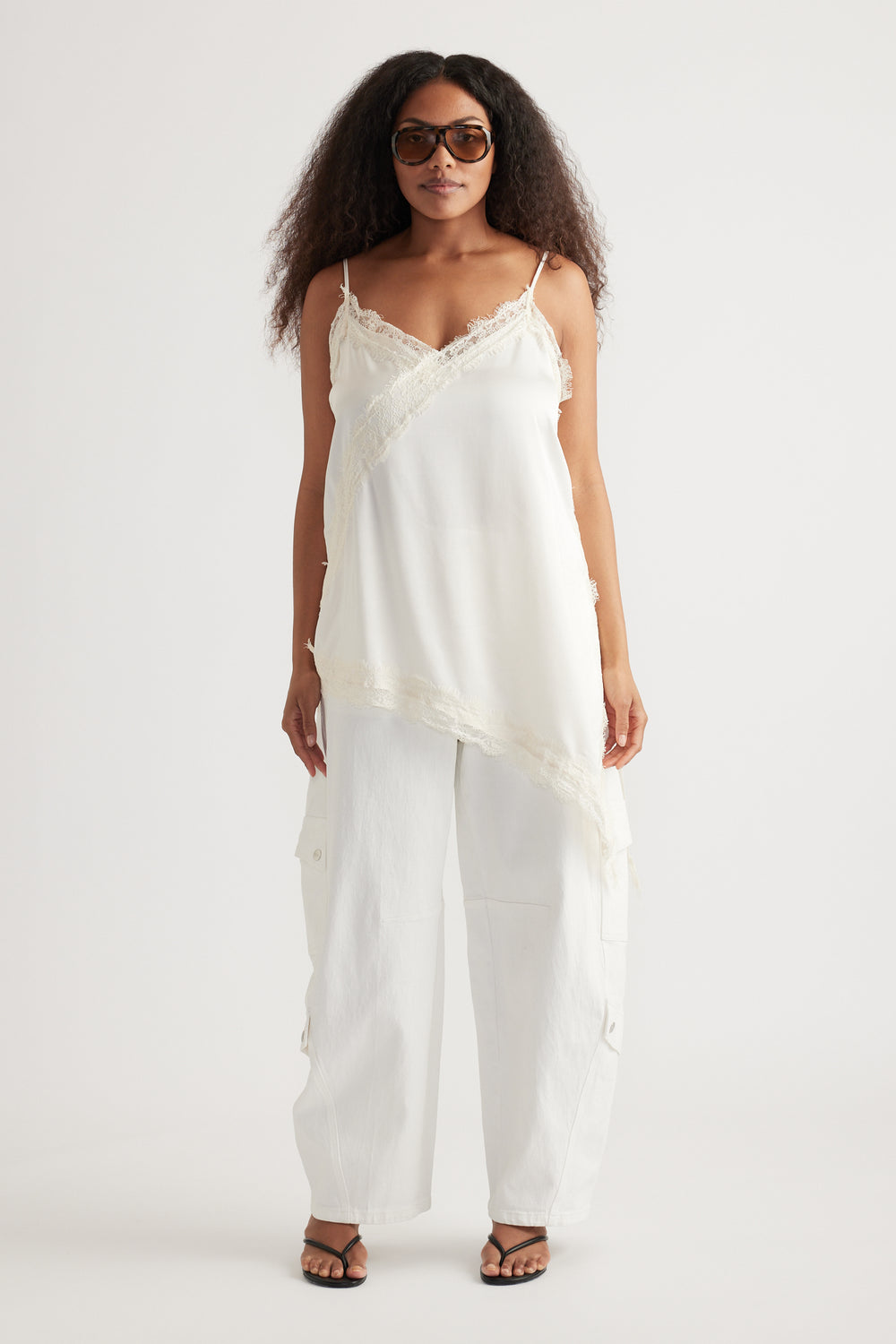 Woman wearing a white lace-trim camisole with relaxed cargo pants, sunglasses and strappy sandals