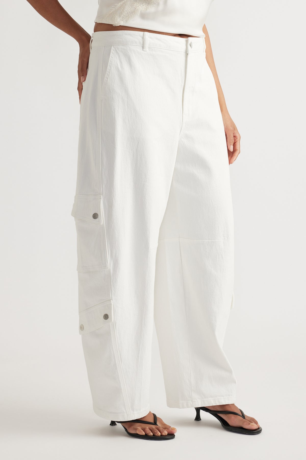 Model wearing white barrel-leg cargo jeans with a cropped top and black sandals