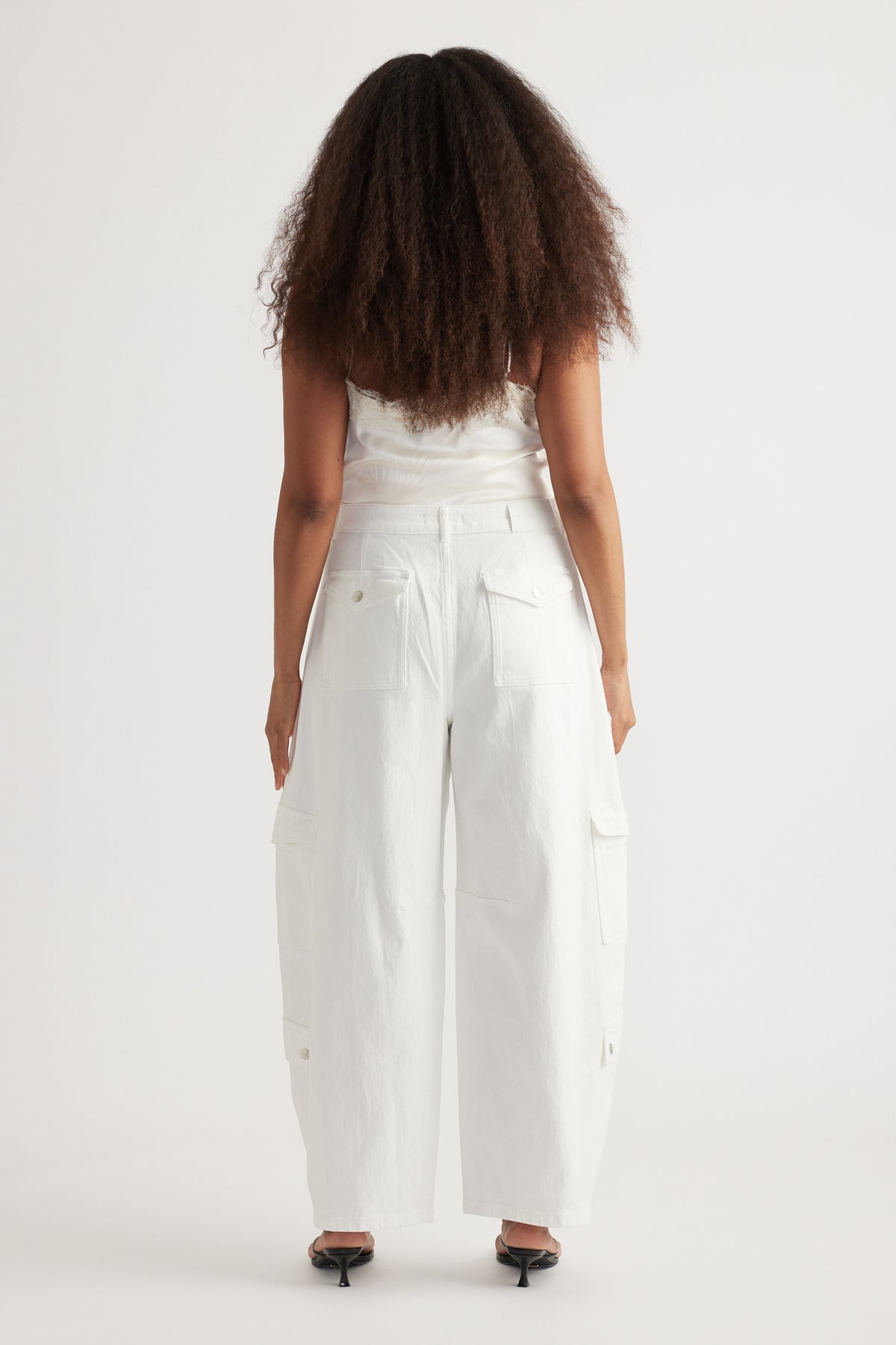 Back view of a woman wearing white cargo barrel-leg jeans, a white top and black heels