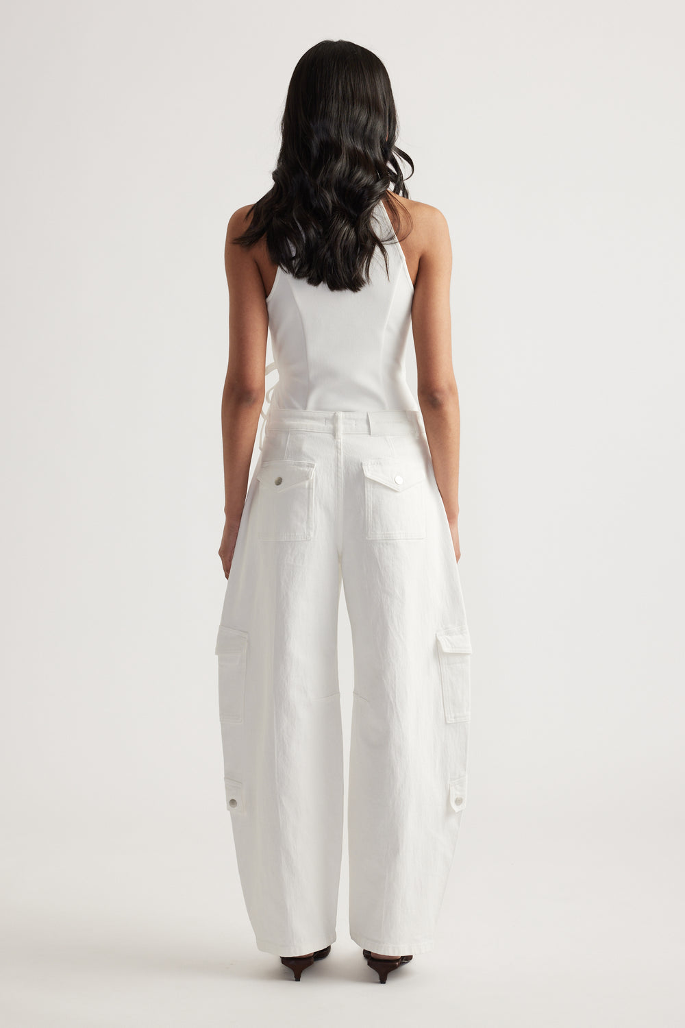 Woman viewed from behind wearing white cargo barrel-leg jeans with a white tank top and heels