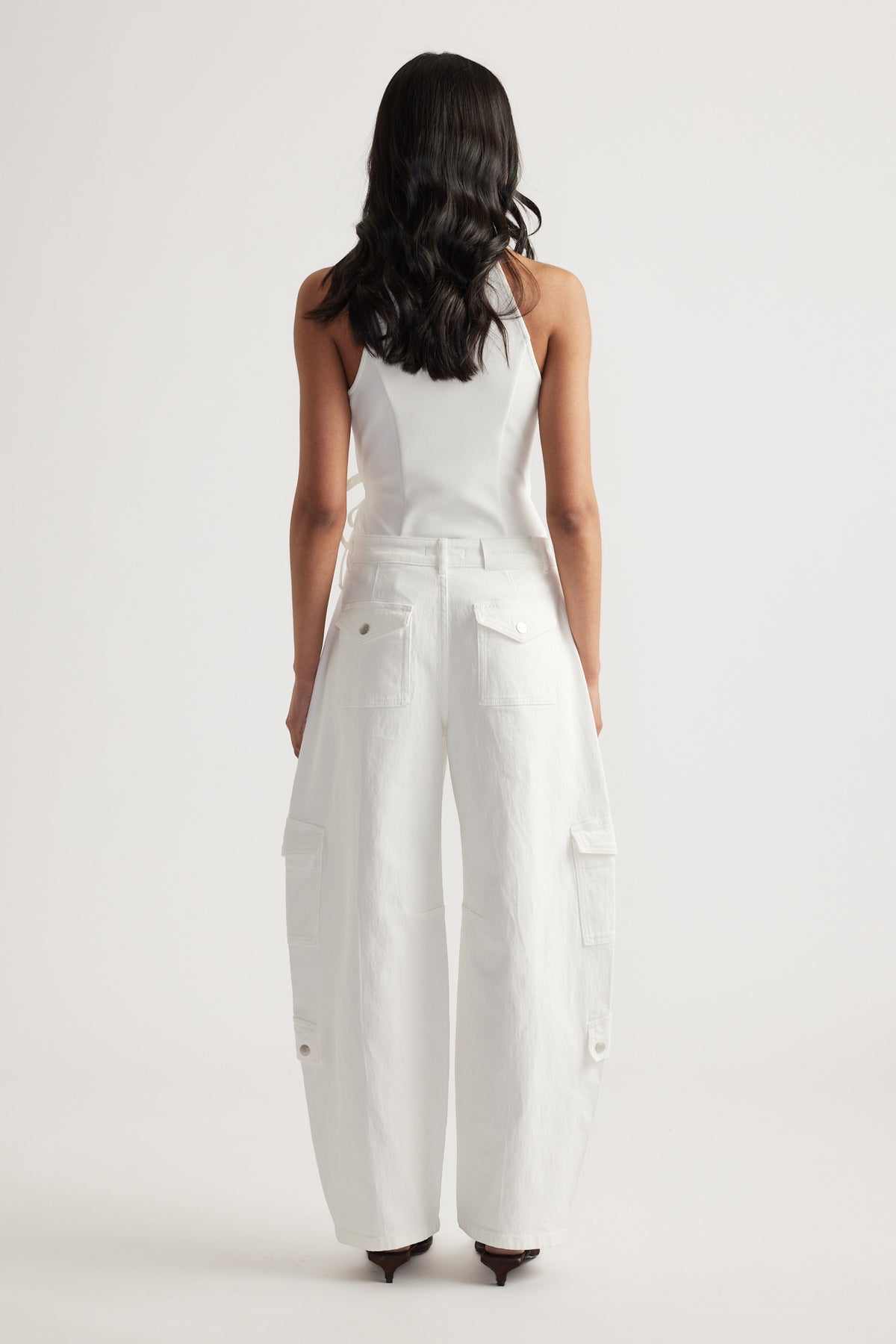 Woman viewed from behind wearing white cargo barrel-leg jeans with a white tank top and heels