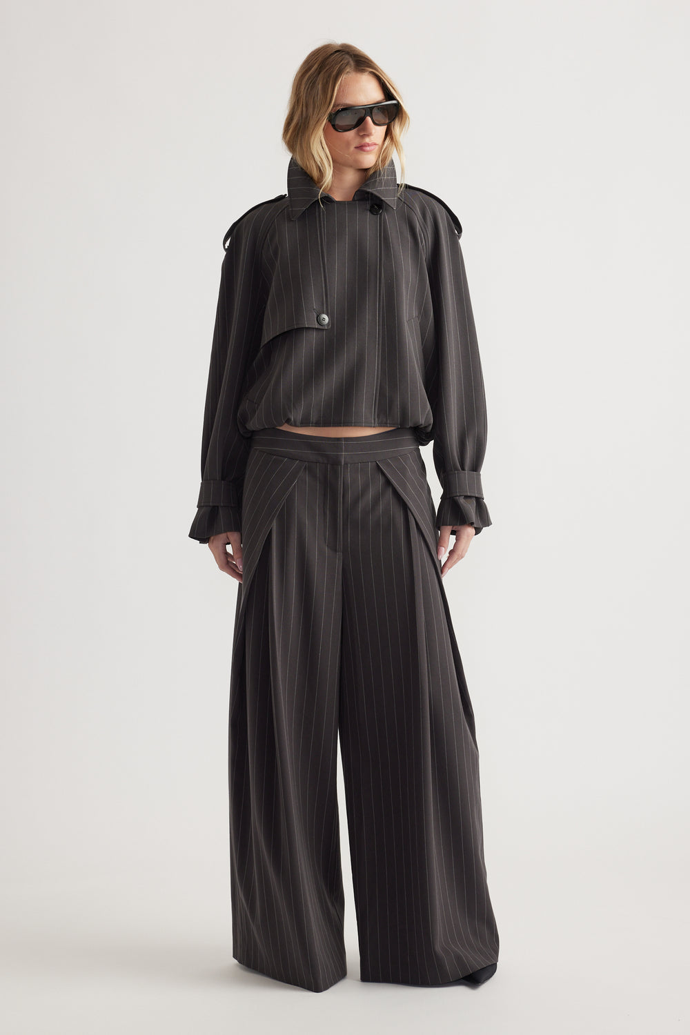 Woman wearing oversized pinstripe blazer with button detail and matching wide-leg pants paired with black sunglasses