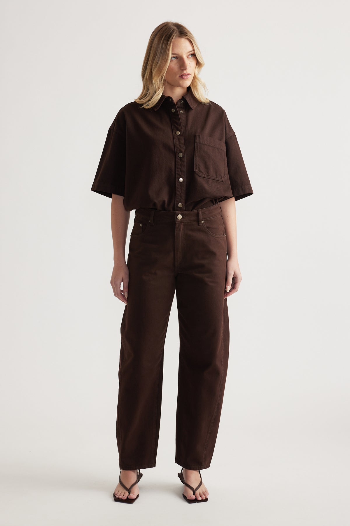 Woman wearing a chocolate brown cropped shirt with matching barrel leg jeans and black strappy sandals