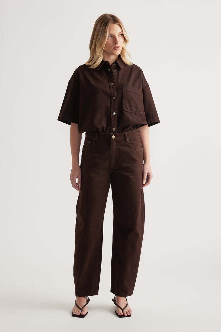 Woman wearing a chocolate brown cropped shirt with matching barrel leg jeans and black strappy sandals