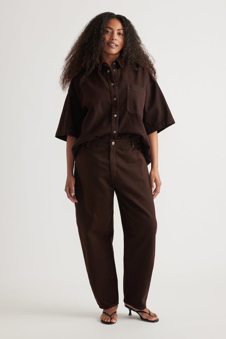 Woman wearing a dark brown oversized shirt with high rise barrel leg jeans and flat sandals