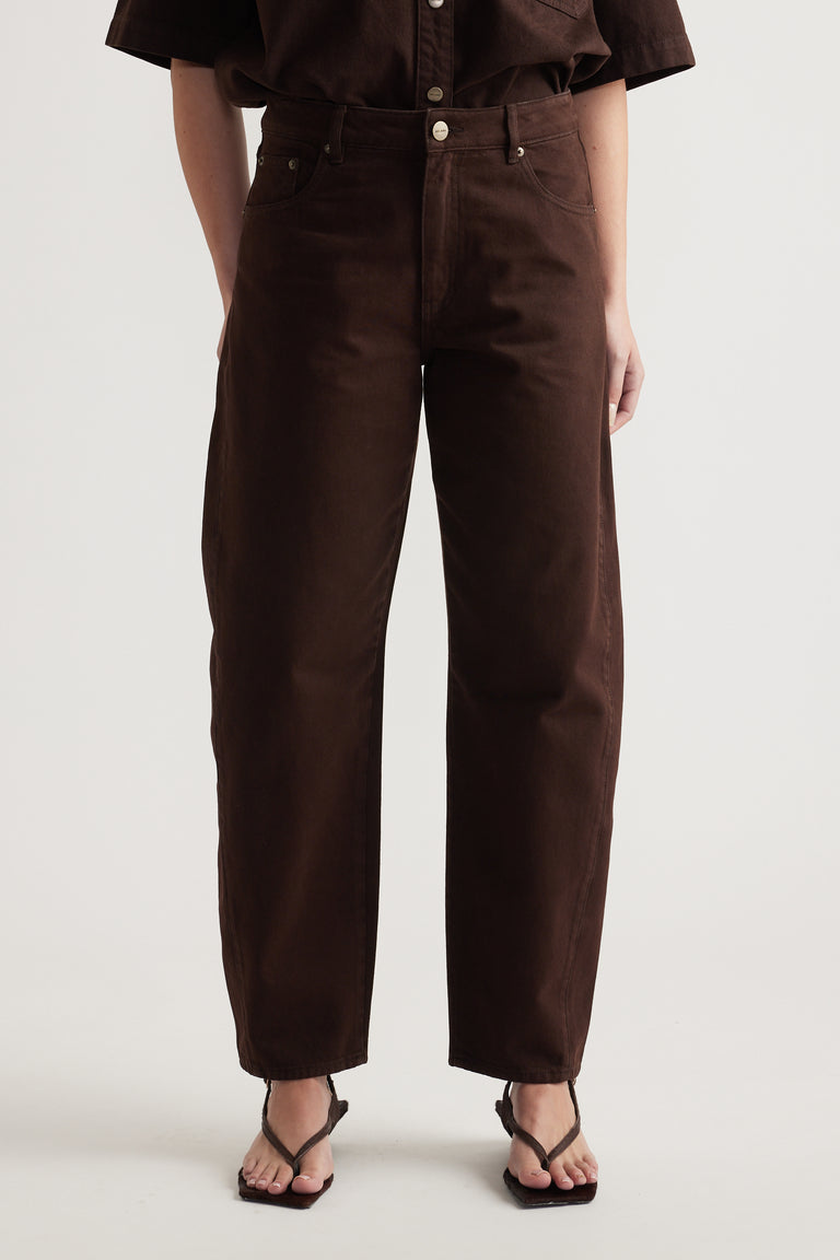 Woman wearing dark brown high rise barrel leg jeans with a cropped shirt and strappy sandals