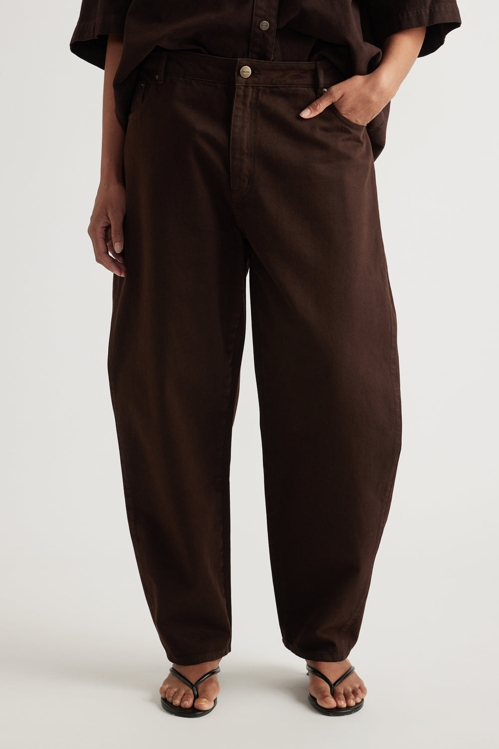 Woman wearing dark brown barrel leg jeans with a matching short sleeve shirt and sandals