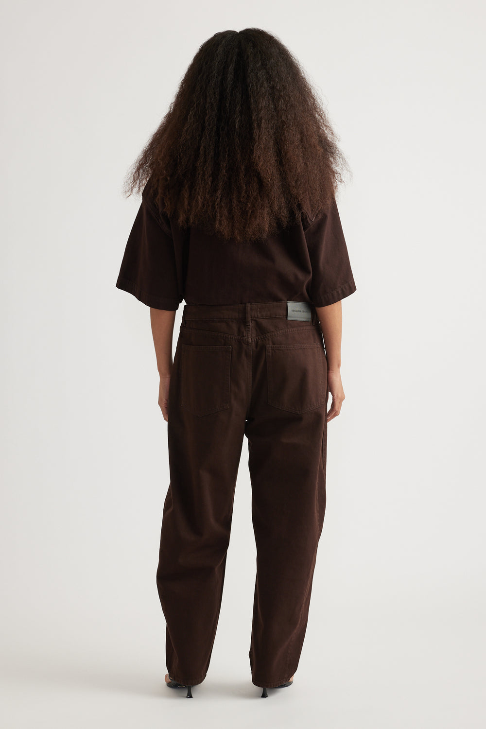 Back view of a model wearing dark brown high-rise barrel leg jeans with a matching oversized top