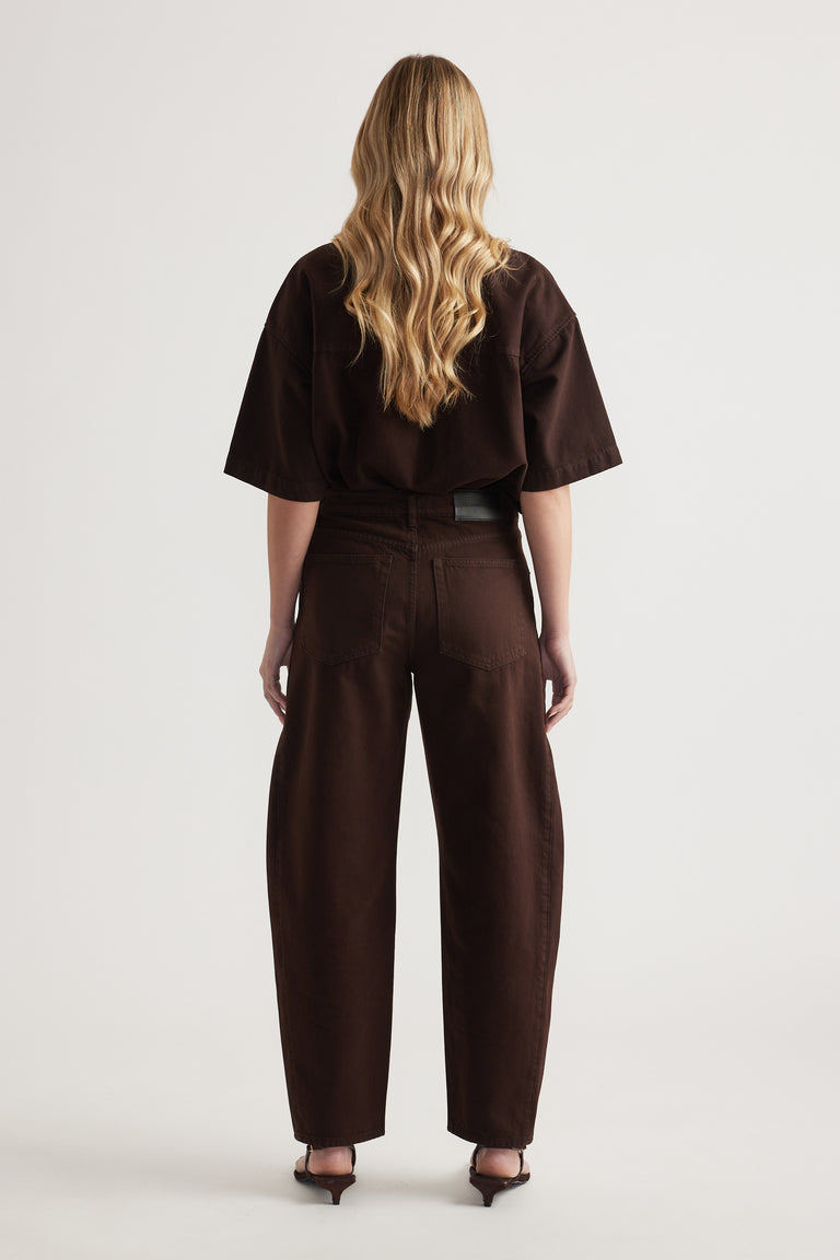 Back view of a woman wearing dark brown barrel leg jeans with a matching oversized tee and heels