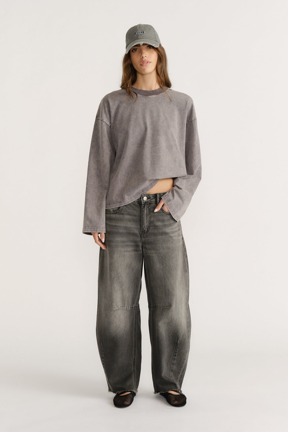 Woman in a cropped grey top, grey cap and dark wash curved wide-leg jeans with black flats