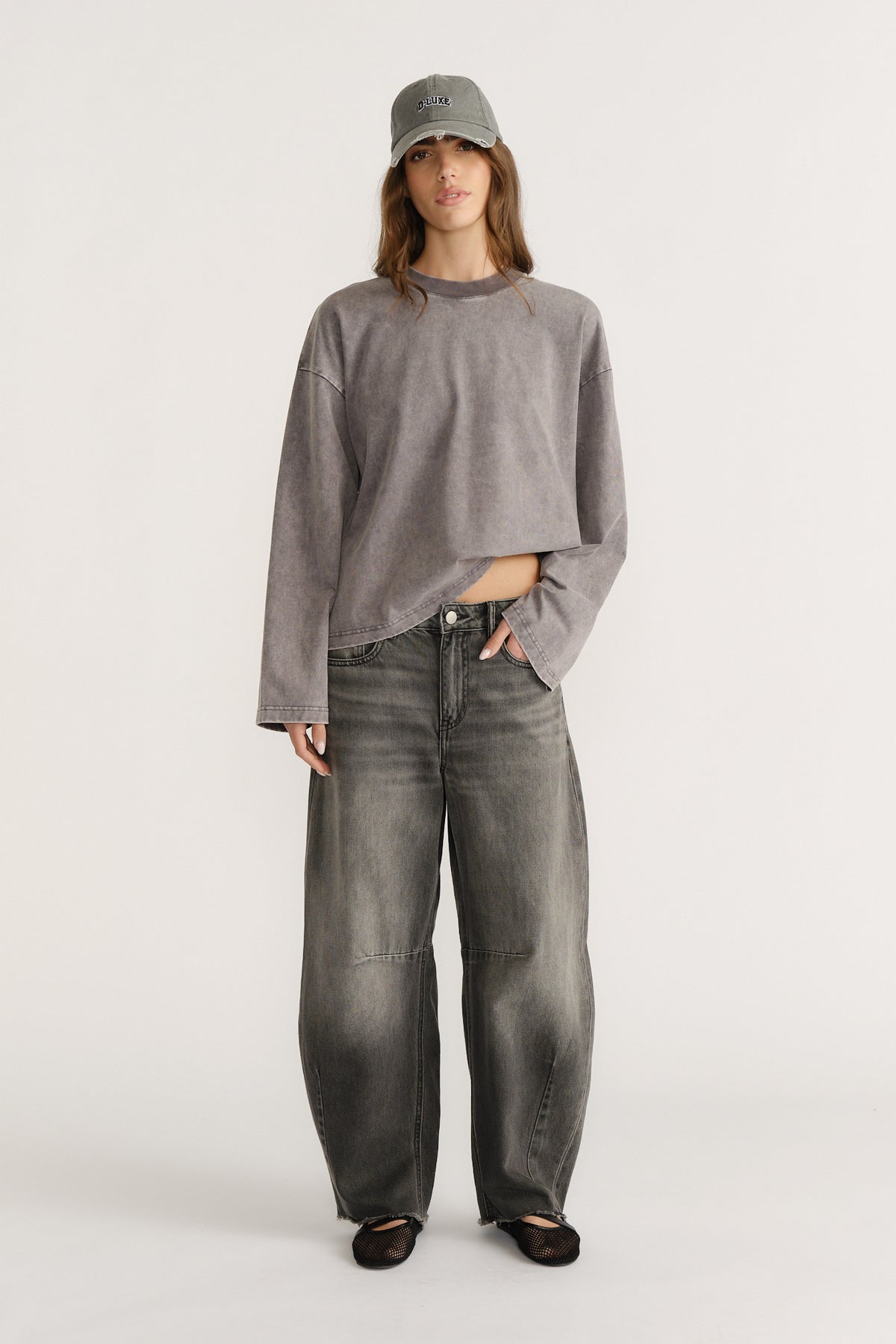 Woman in a cropped grey top, grey cap and dark wash curved wide-leg jeans with black flats