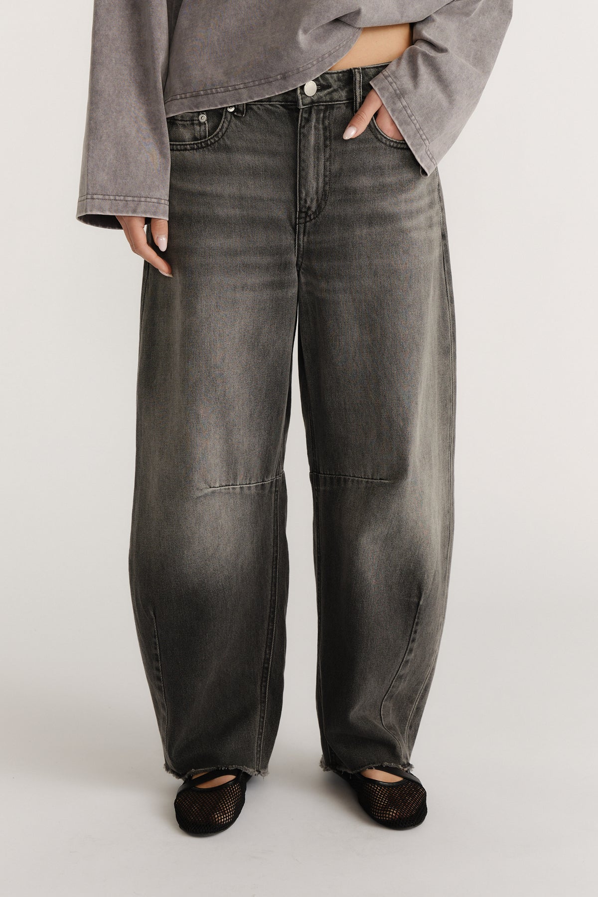 Model wearing charcoal grey horseshoe jeans with curved wide legs and black mesh flats