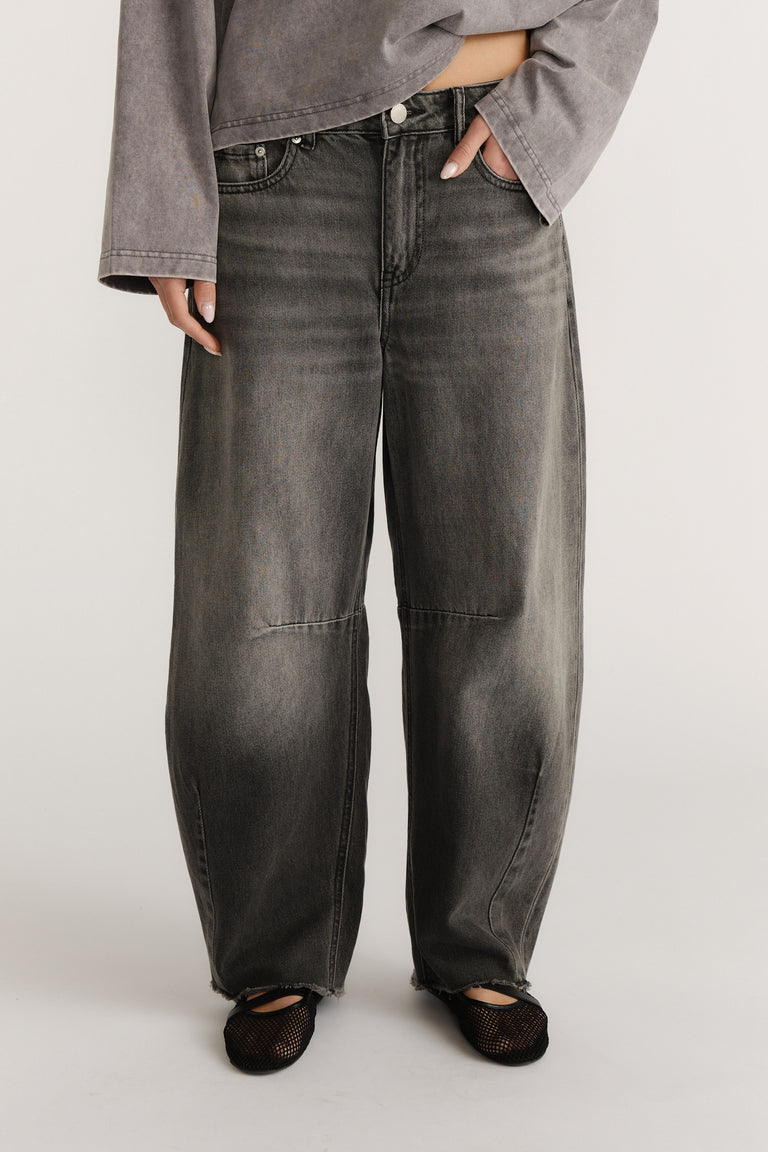 Model wearing charcoal grey horseshoe jeans with curved wide legs and black mesh flats