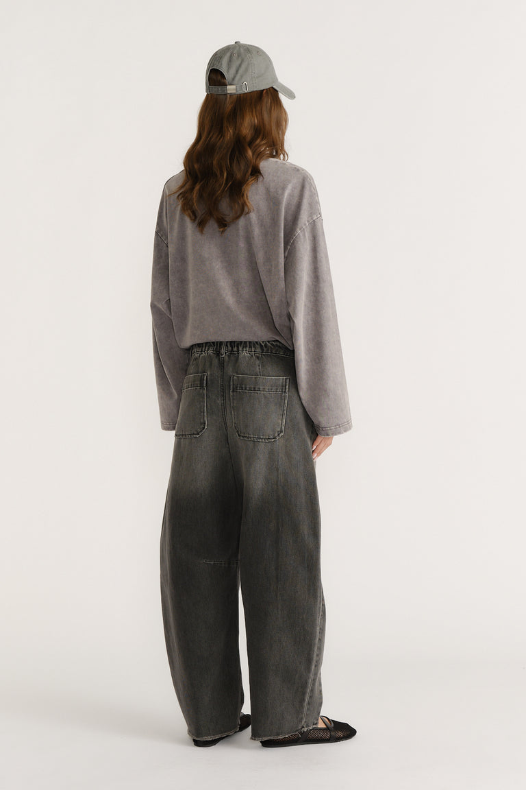 Back view of model in charcoal horseshoe jeans, a grey long sleeve top, baseball cap and pointed flats