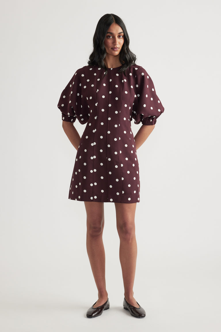 Woman wearing a burgundy polka dot mini dress with puff sleeves and a crew neck