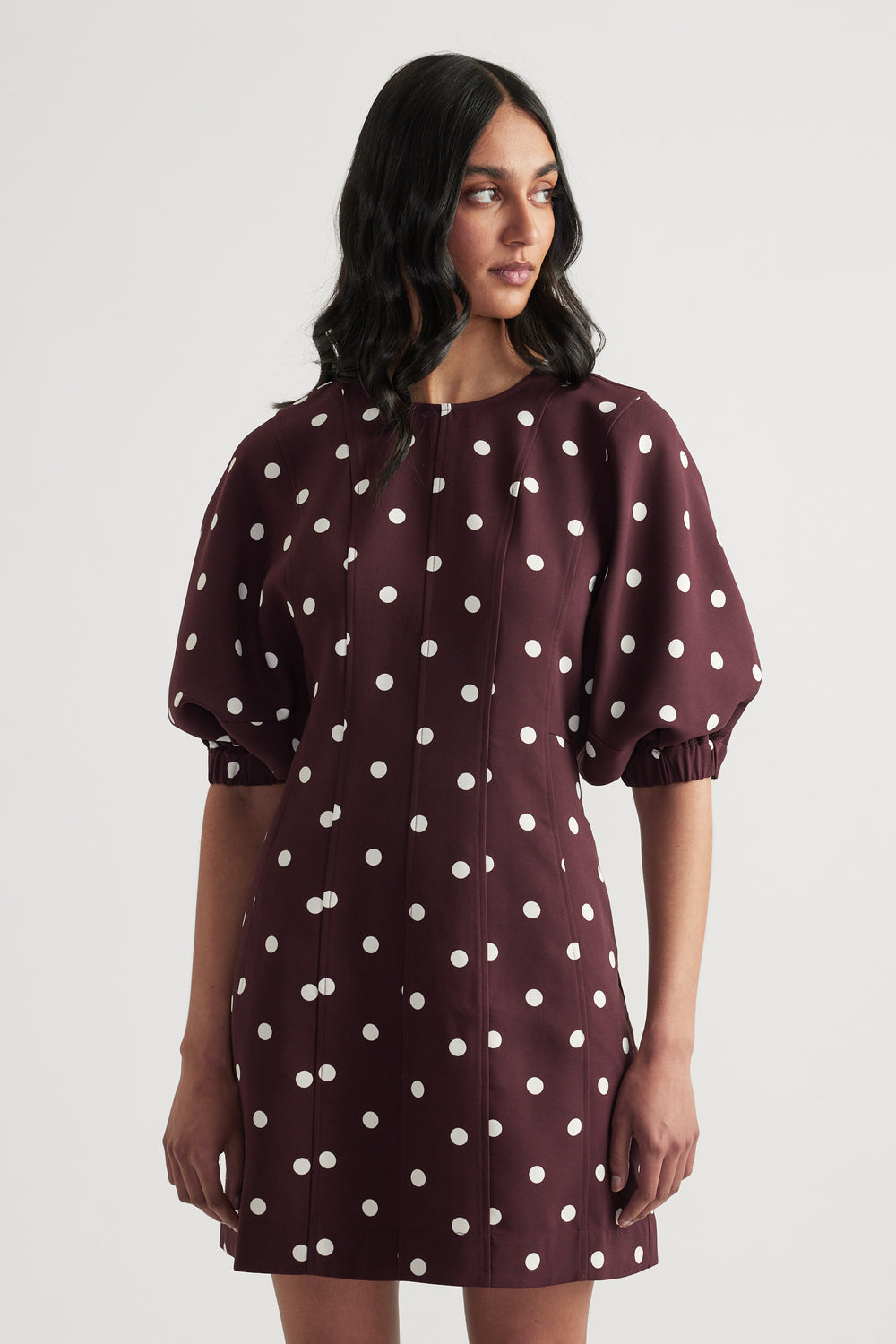 Woman wearing a burgundy polka dot mini dress with puff sleeves and a crew neck