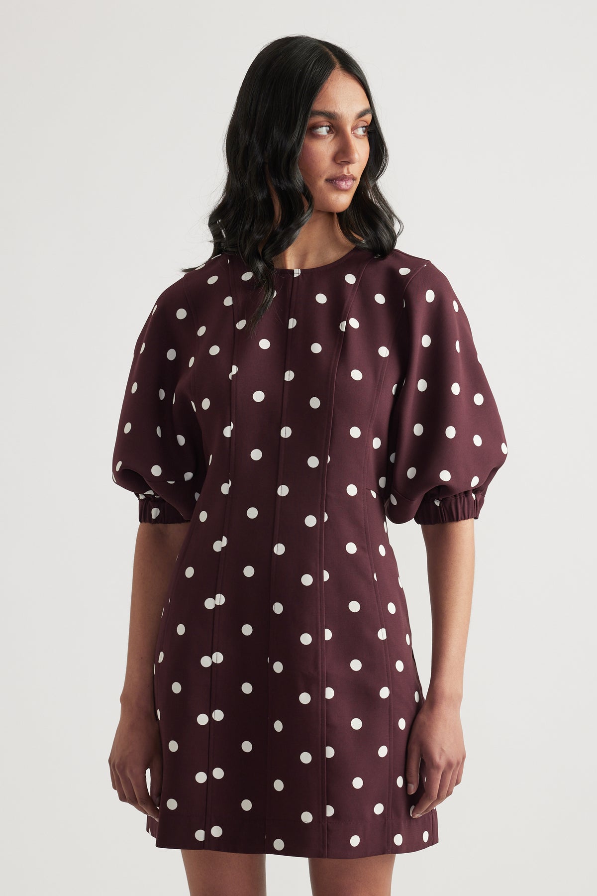 Woman wearing a burgundy polka dot mini dress with puff sleeves and a crew neck