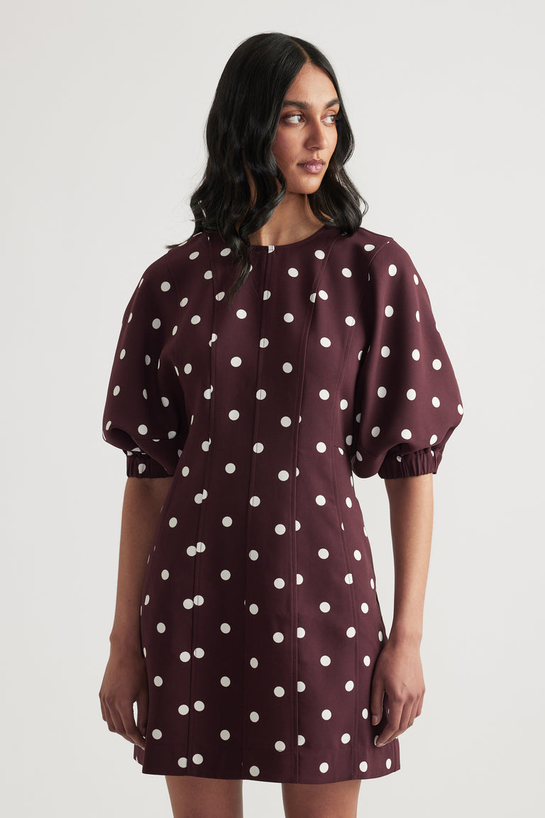 Woman wearing a burgundy polka dot mini dress with puff sleeves and a crew neck