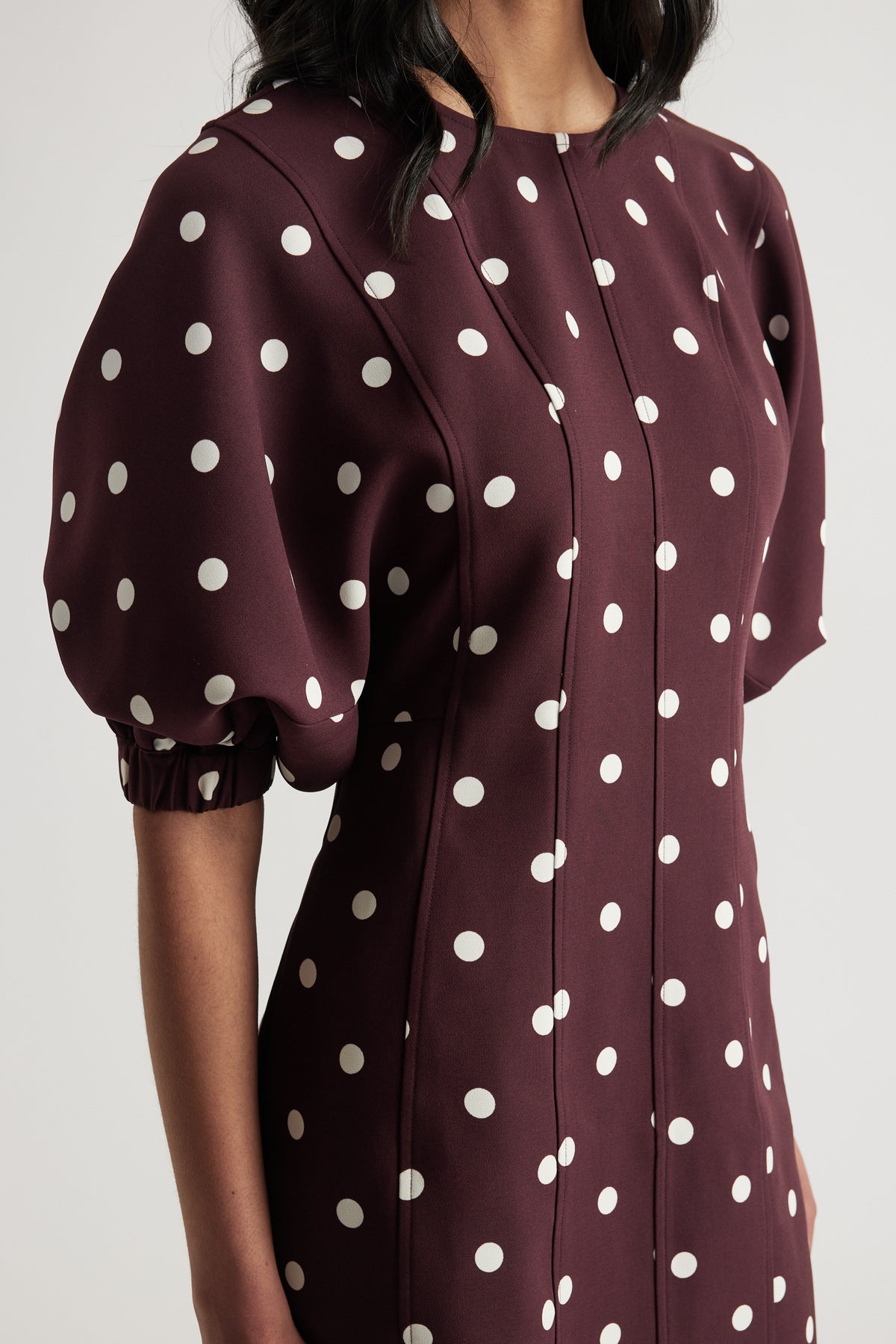 Woman wearing a burgundy mini dress with white polka dots, puff sleeves and a crew neck