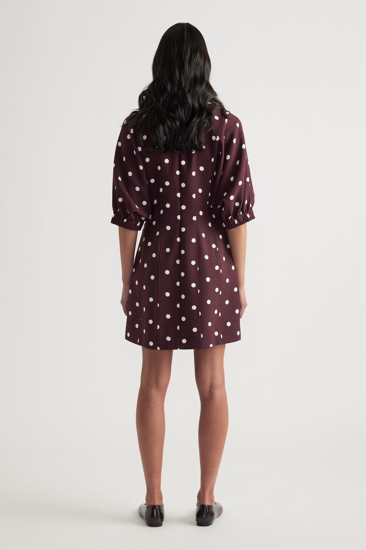 Woman wearing a burgundy polka dot mini dress with puff sleeves and a cinched waist
