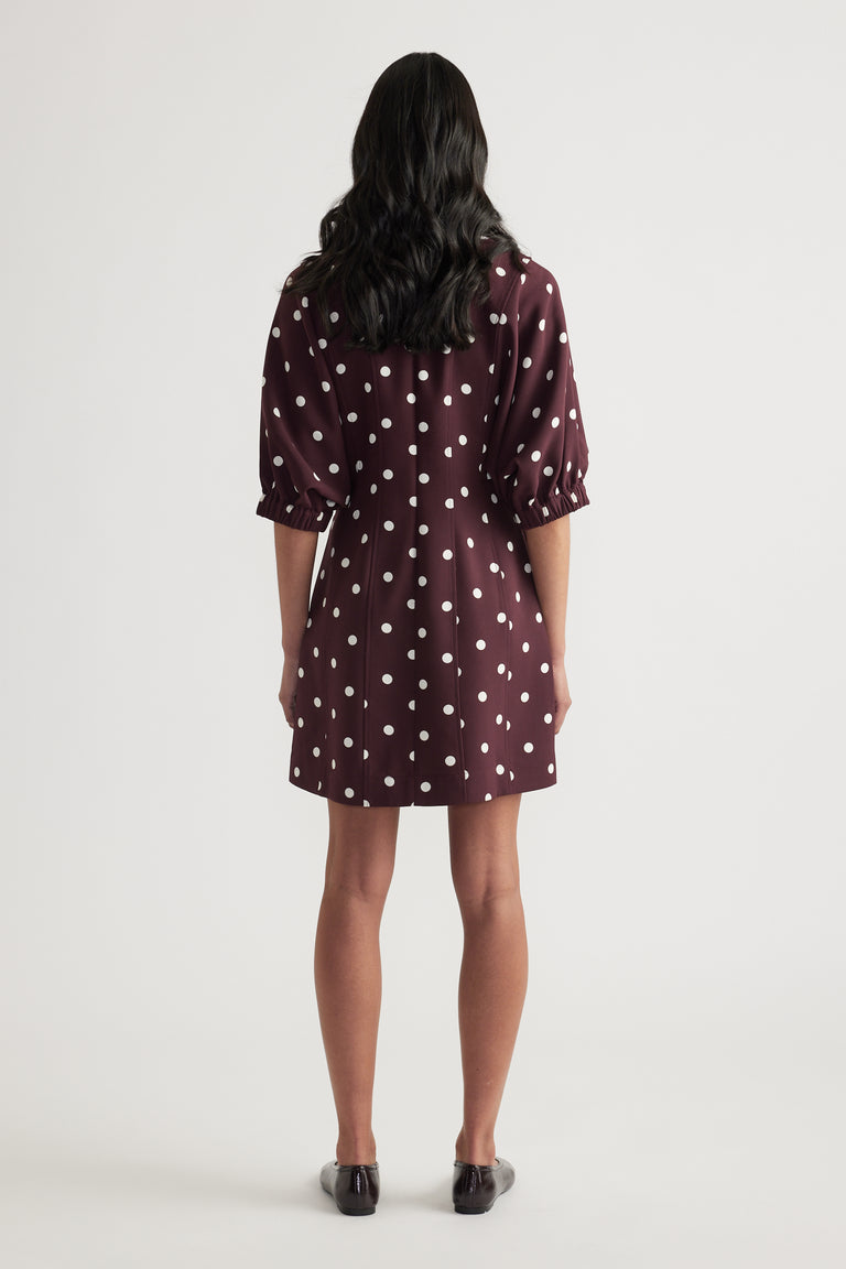 Woman wearing a burgundy polka dot mini dress with puff sleeves and a cinched waist