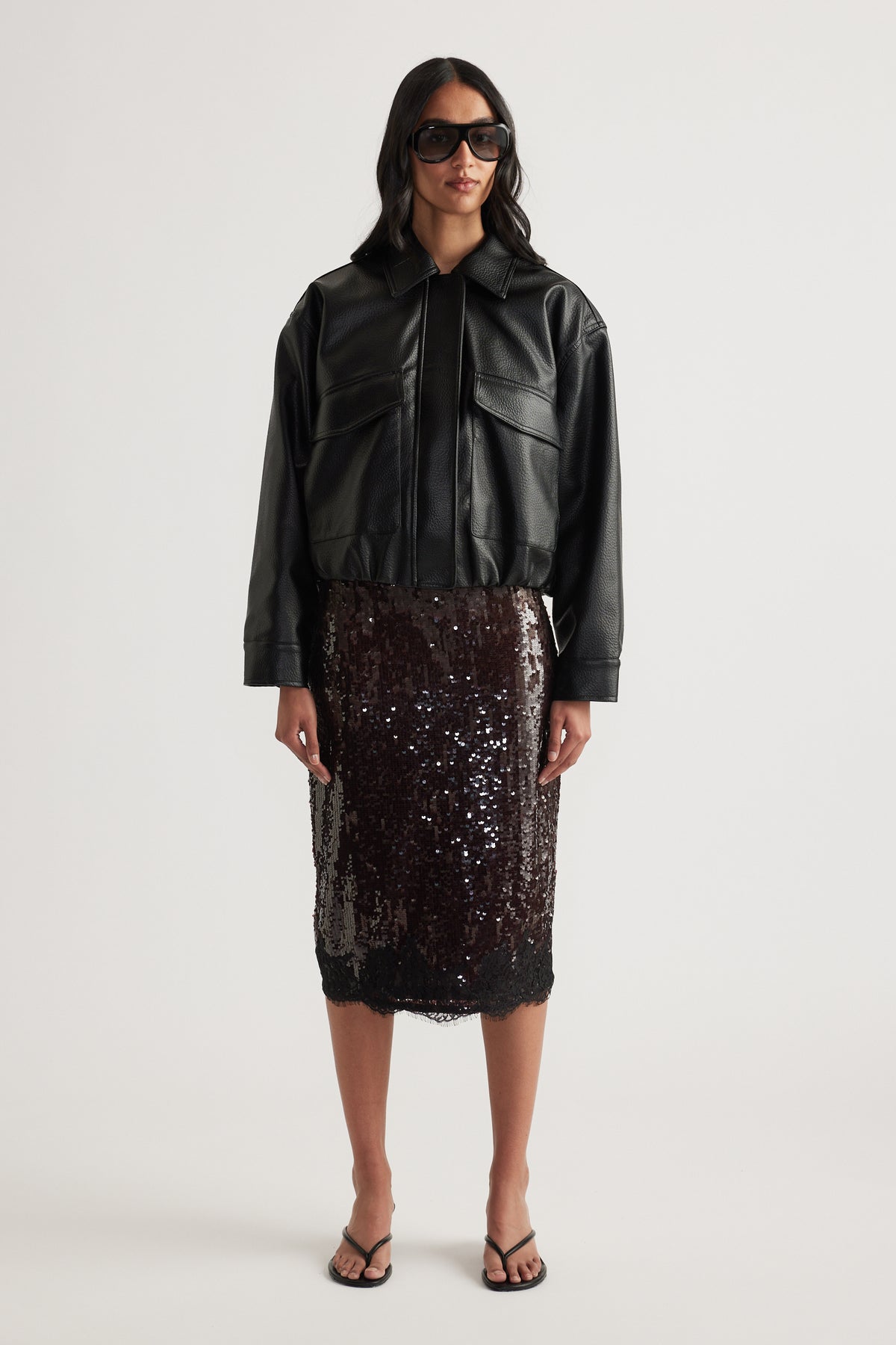 Woman styling a black sequin knee-length skirt with a cropped leather jacket and sandals