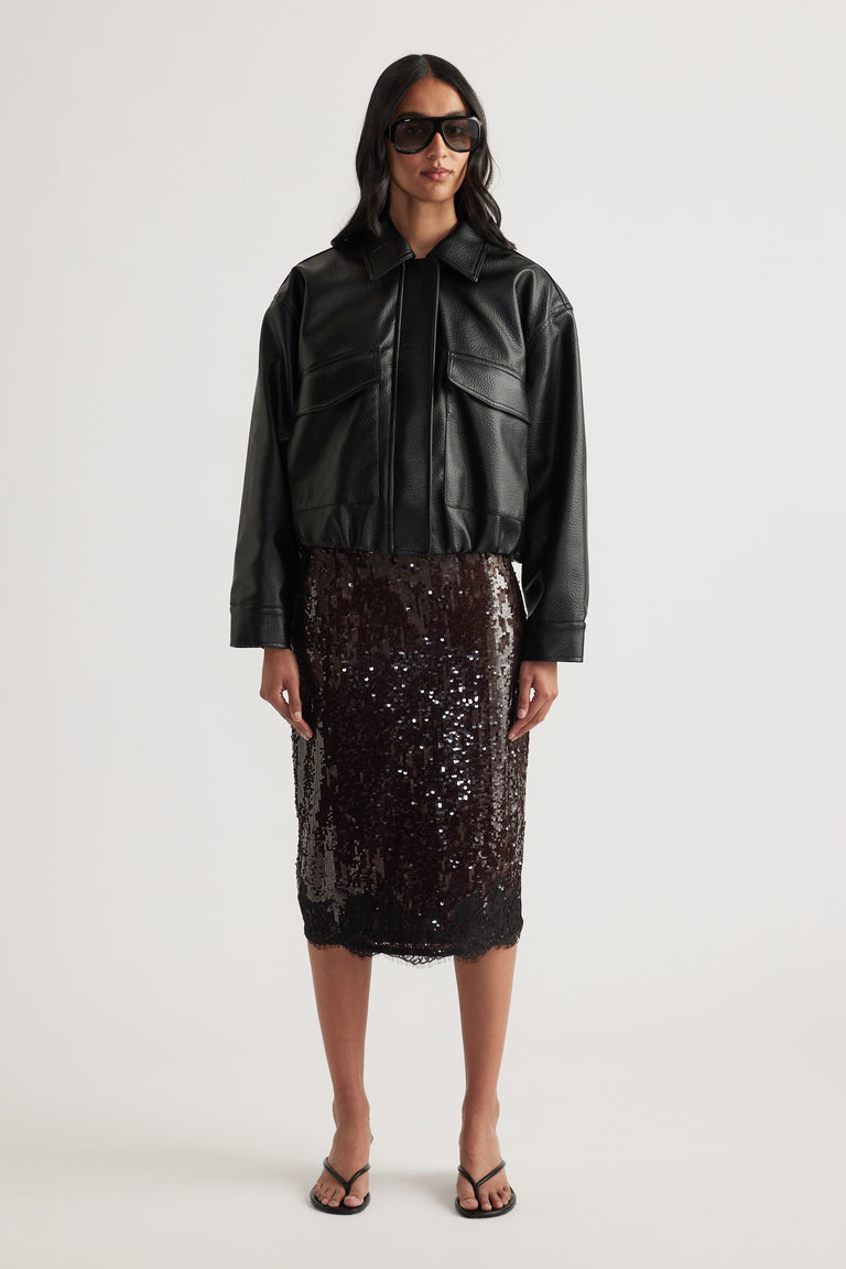 Woman styling a black sequin knee-length skirt with a cropped leather jacket and sandals