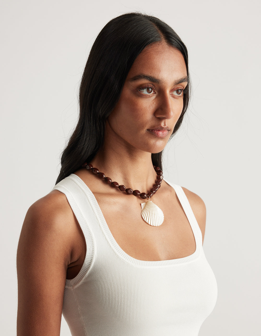 Woman wearing a white ribbed tank top and chocolate stone necklace with a shell pendant