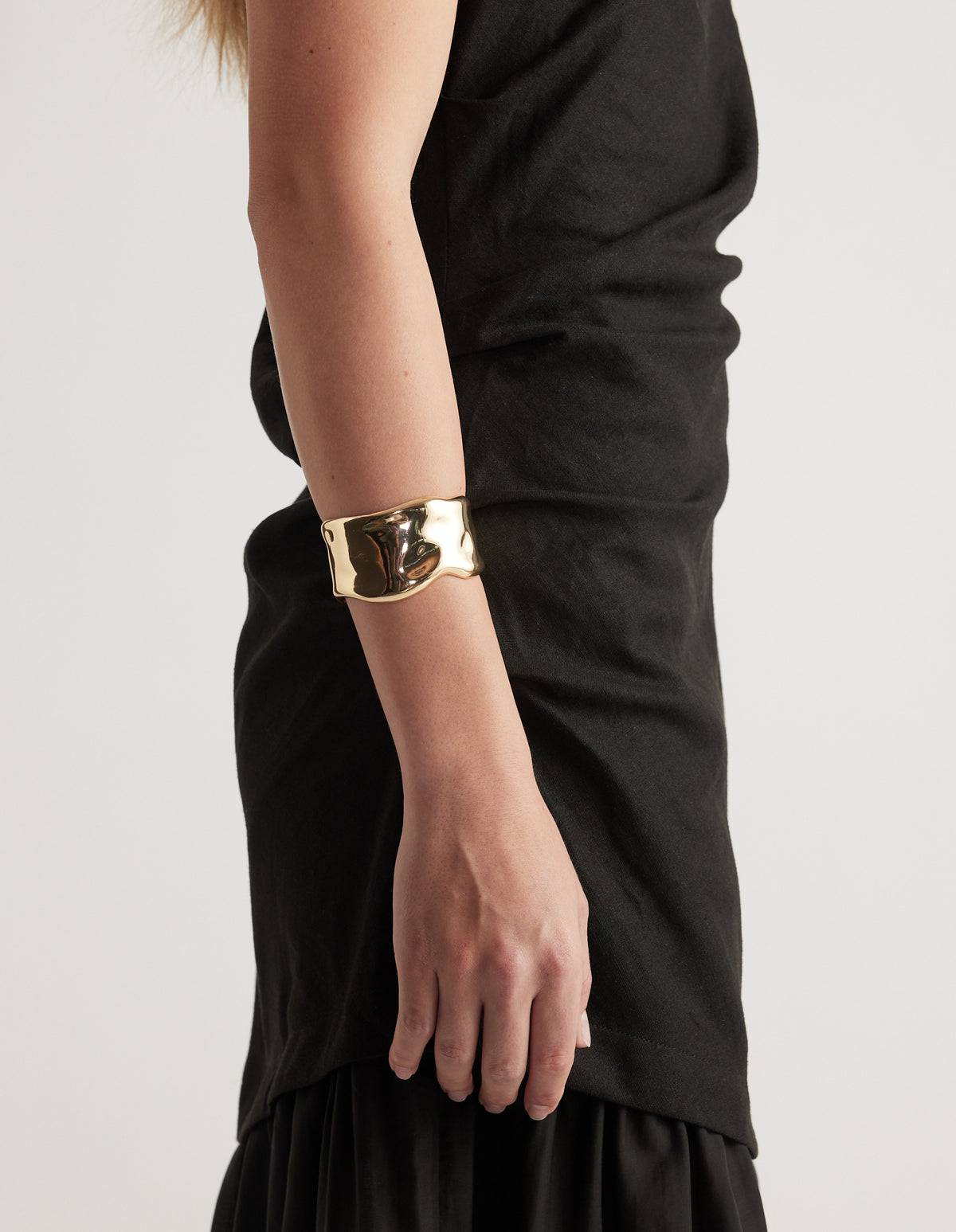 Woman wearing a wide gold cuff bracelet with curved edges and an open back over a black dress