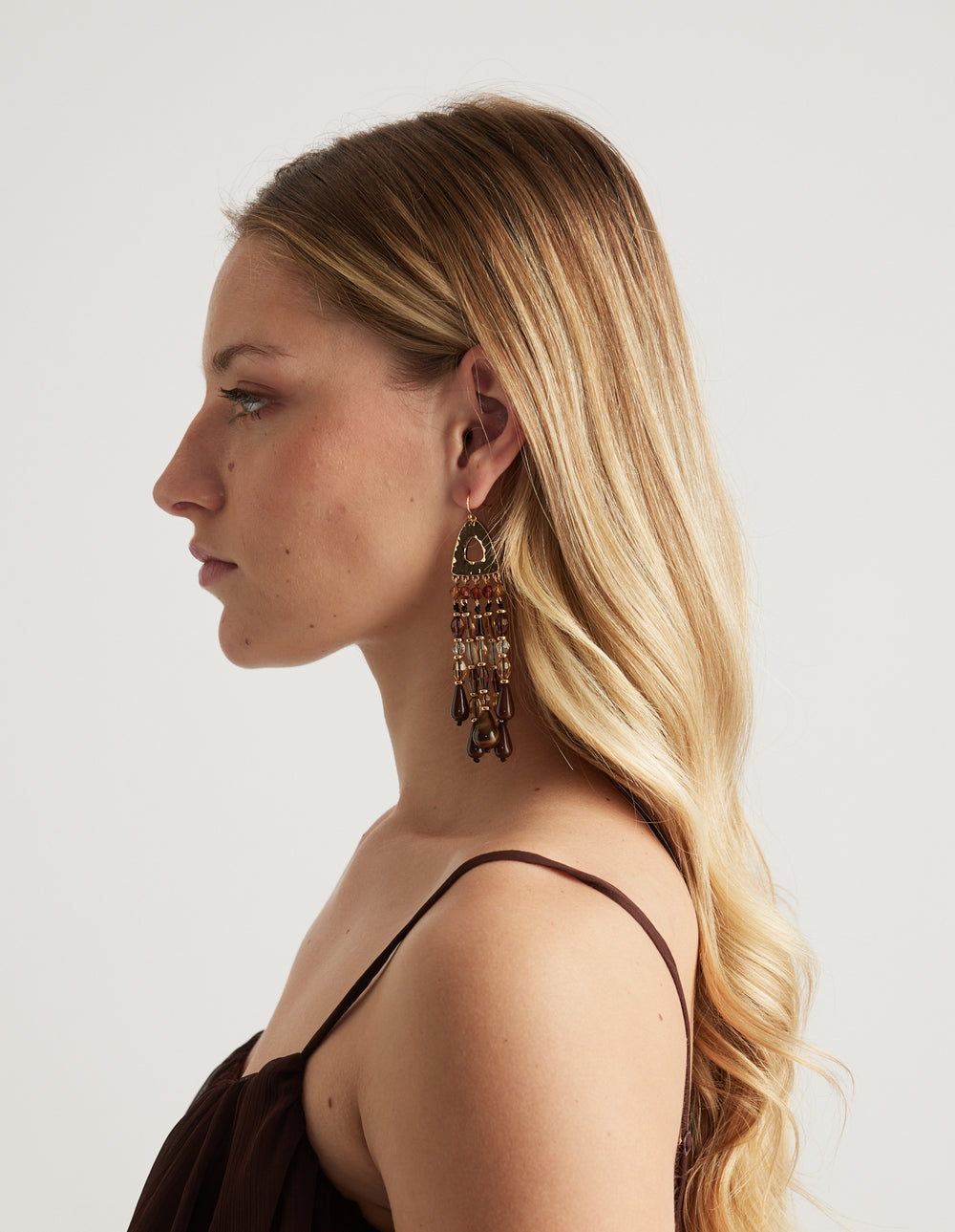Woman wearing a statement earring with a smooth gold top and multicoloured beads