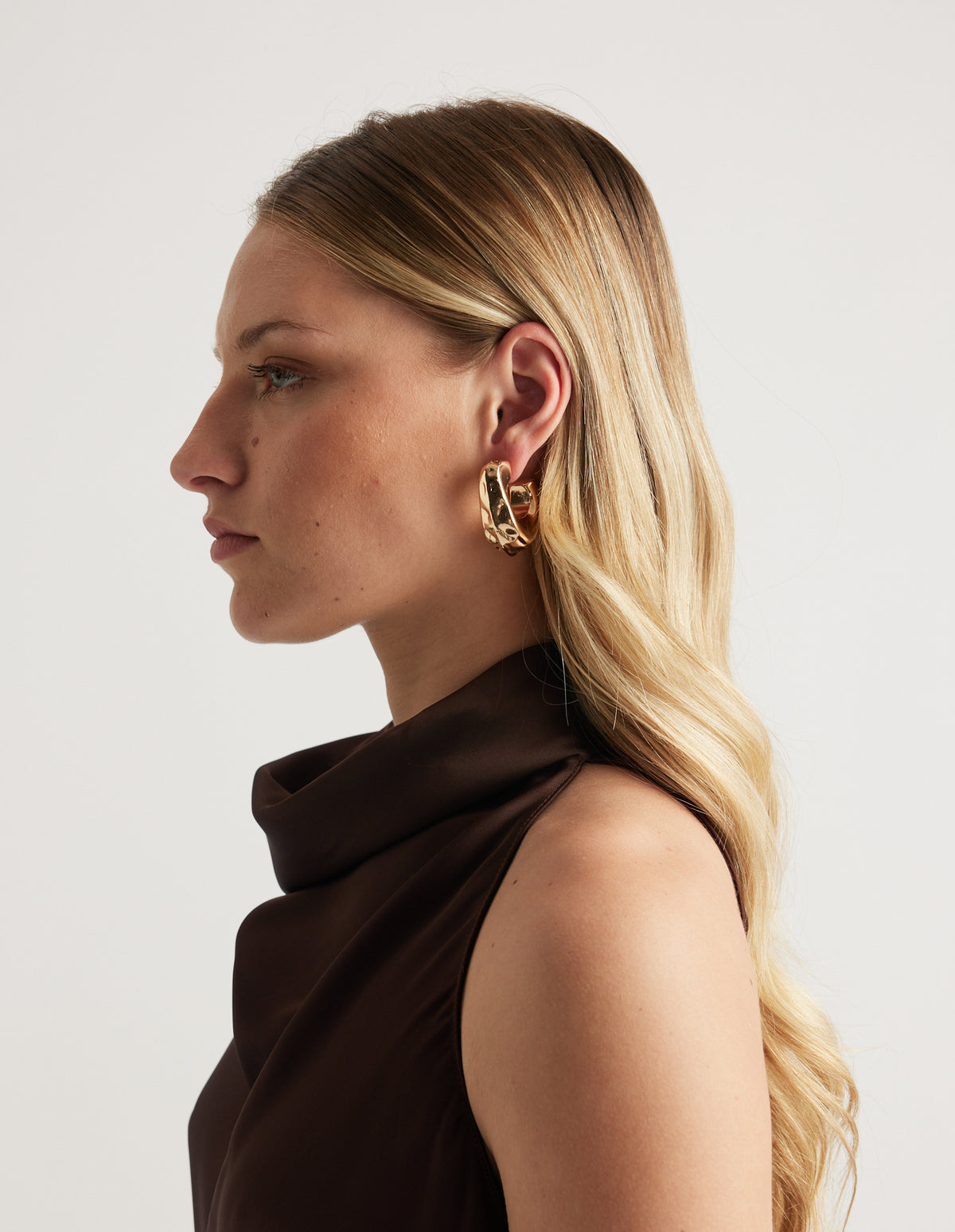 Side profile of a woman wearing a shiny gold open teardrop hoop earring