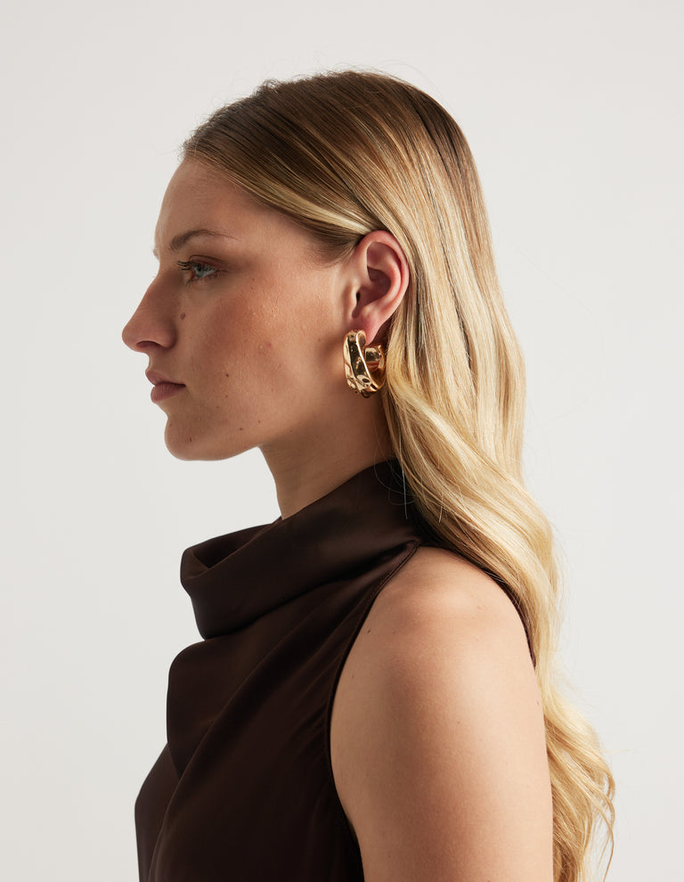 Side profile of a woman wearing a shiny gold open teardrop hoop earring