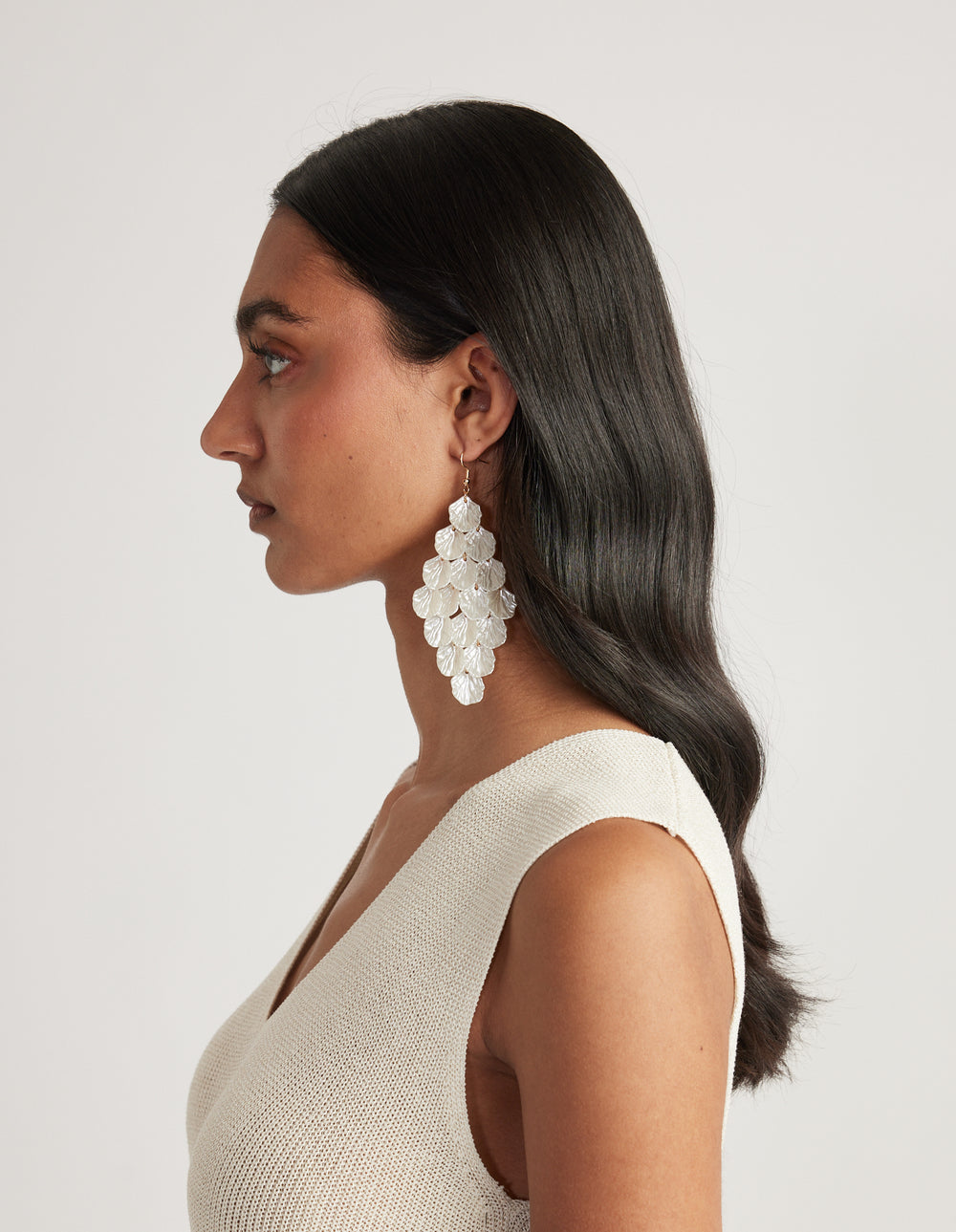 Side profile of woman wearing large layered pearlescent shell drop earrings