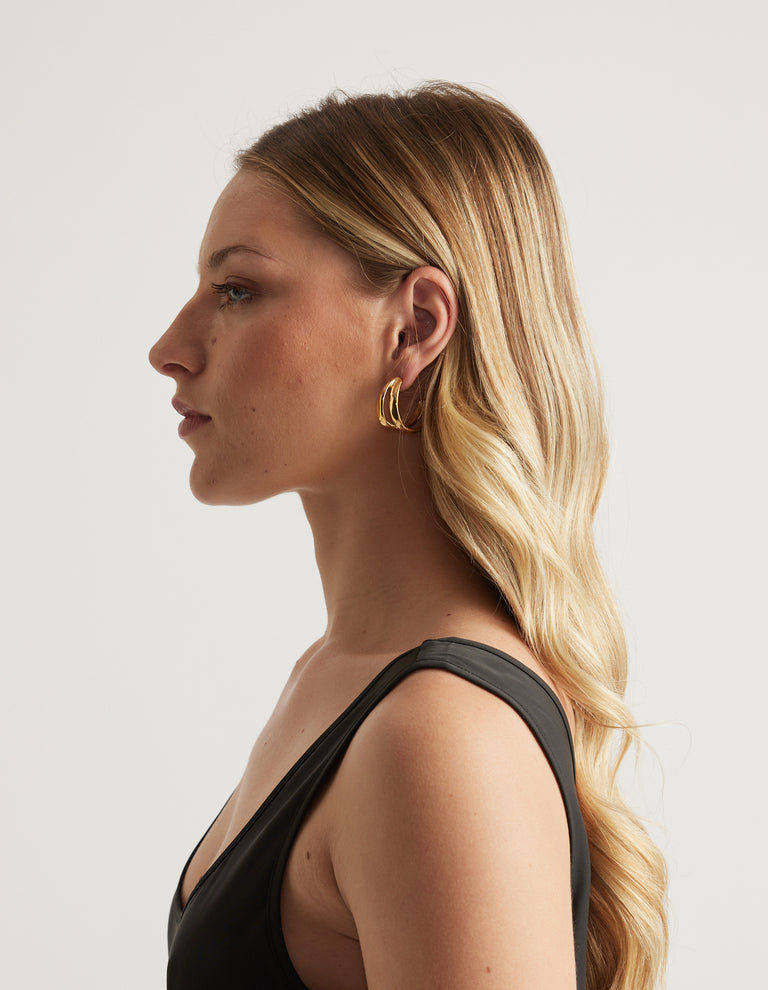 Profile view of a woman wearing gold molten hoop earrings with a black top