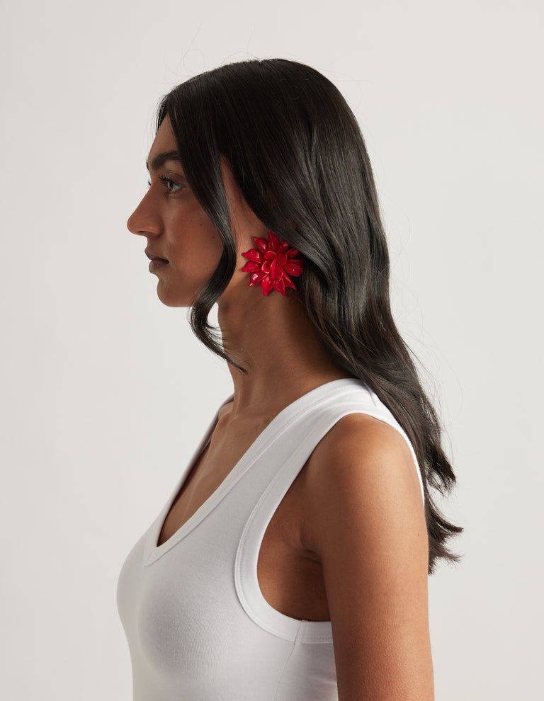 Woman in profile wearing a high shine red flower stud earring with shaped petals and a white tank top